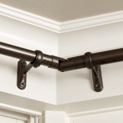 a close up of a curtain rod on a white wall with dark brown metal hardware