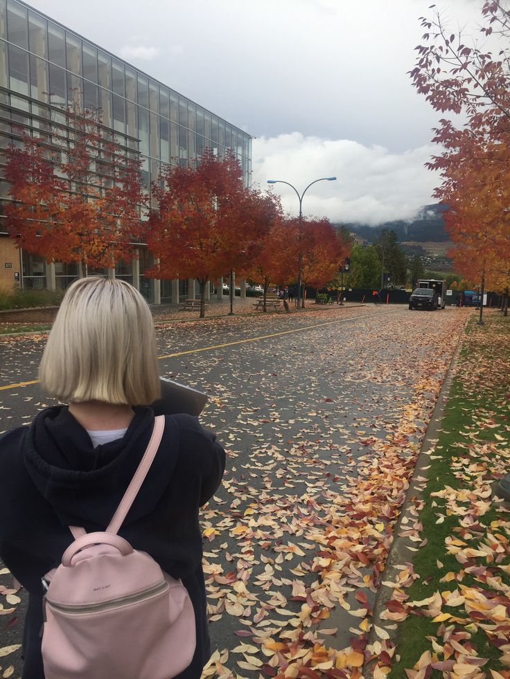 a woman is standing in the middle of an empty street with leaves all over her