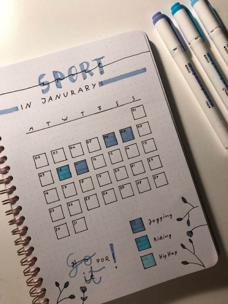 an open planner with blue ink and some pens on it next to two markers that say sport