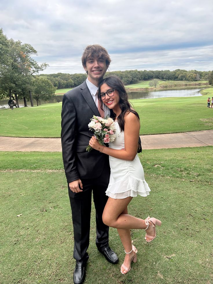 a man and woman posing for a photo in front of a golf course with flowers