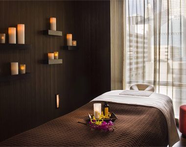 a massage room with candles on the wall and a bed in the foreground next to a window