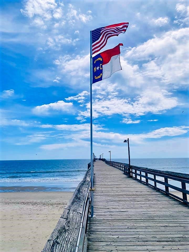 an american flag is flying at the end of a pier near the ocean on a sunny day