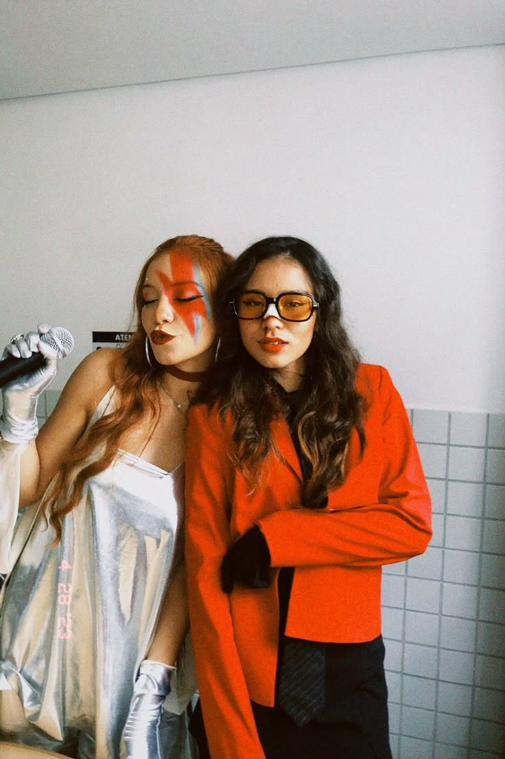 two women with painted faces standing next to each other in front of a bathroom mirror