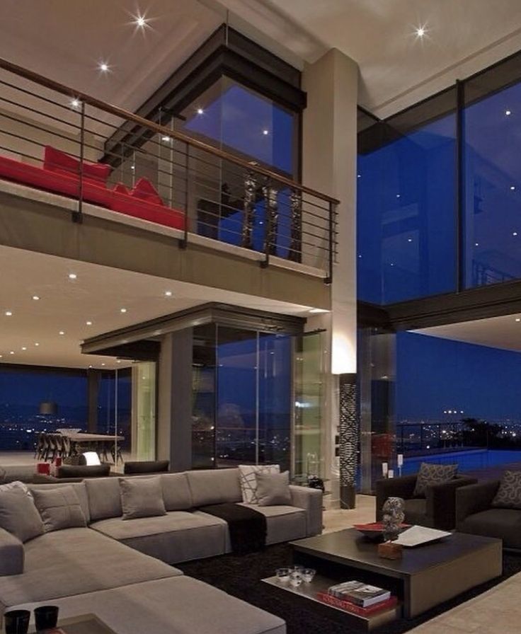 a living room filled with lots of furniture next to tall glass windows at night time