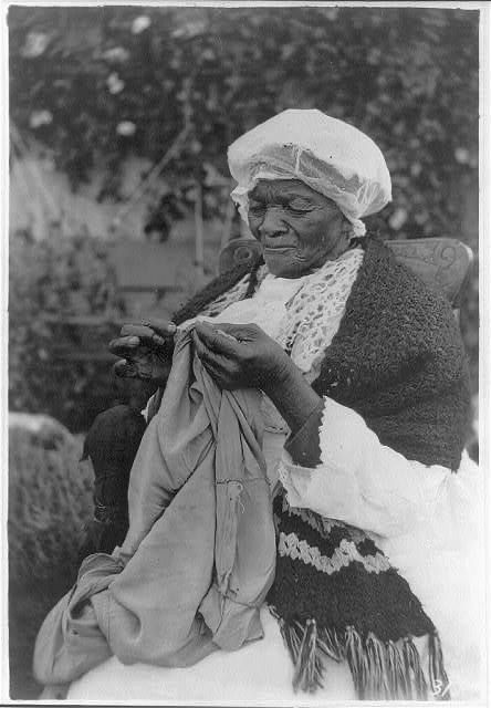 an old black and white photo of a woman sitting on a bench with a scarf around her neck