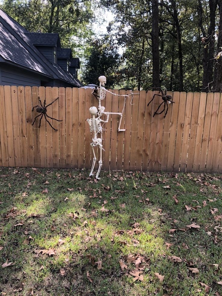 a skeleton is standing in the yard next to a fence with spider webs on it