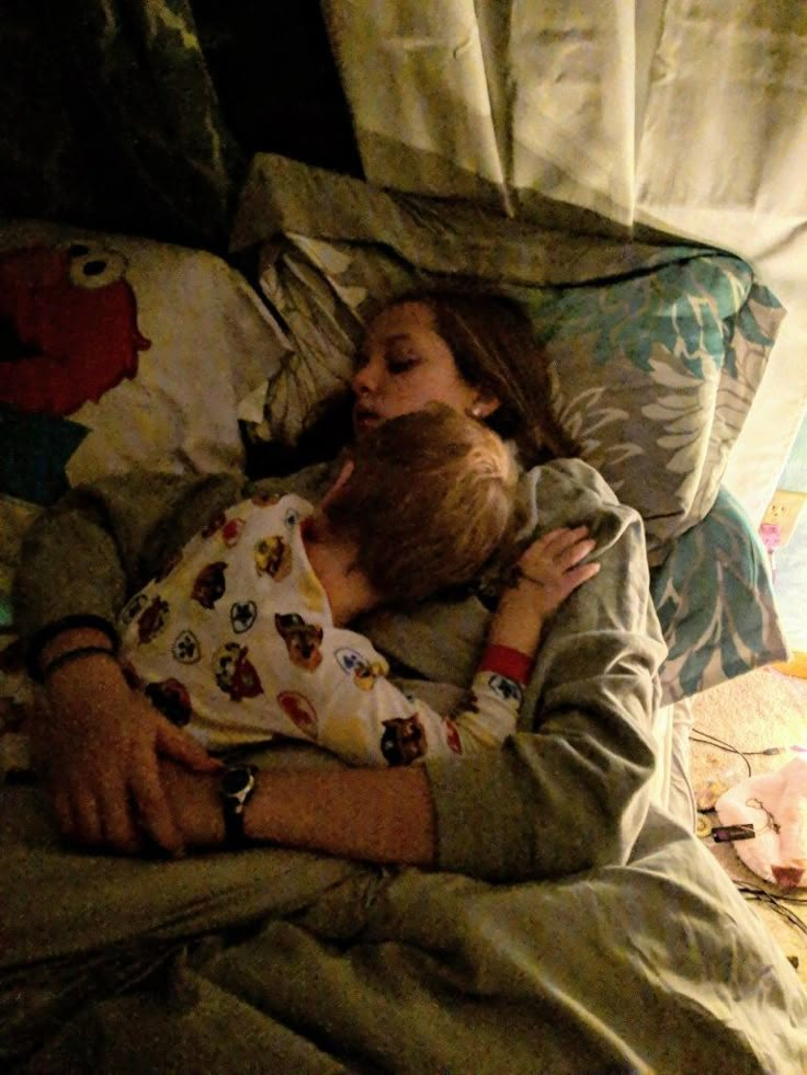 a woman laying in bed with a child sleeping on her back and holding the baby