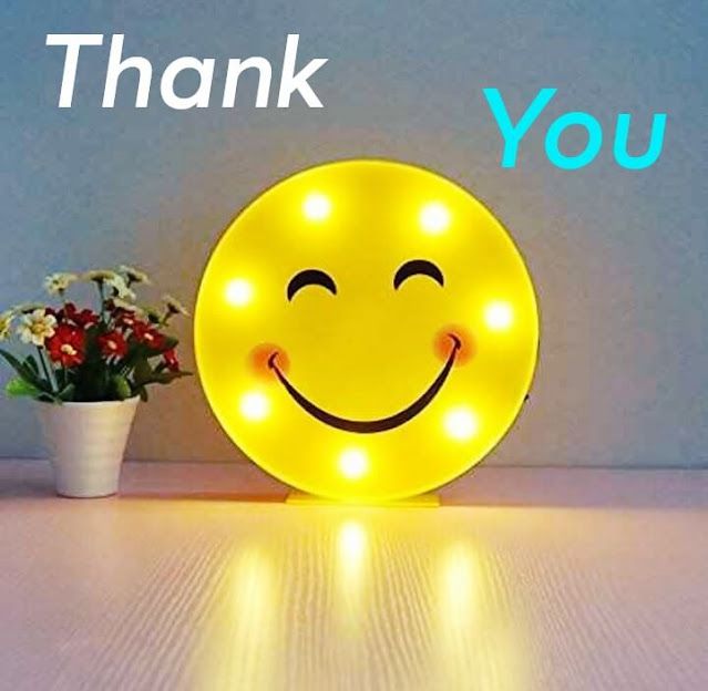 a yellow smiley face light sitting on top of a table next to a potted plant