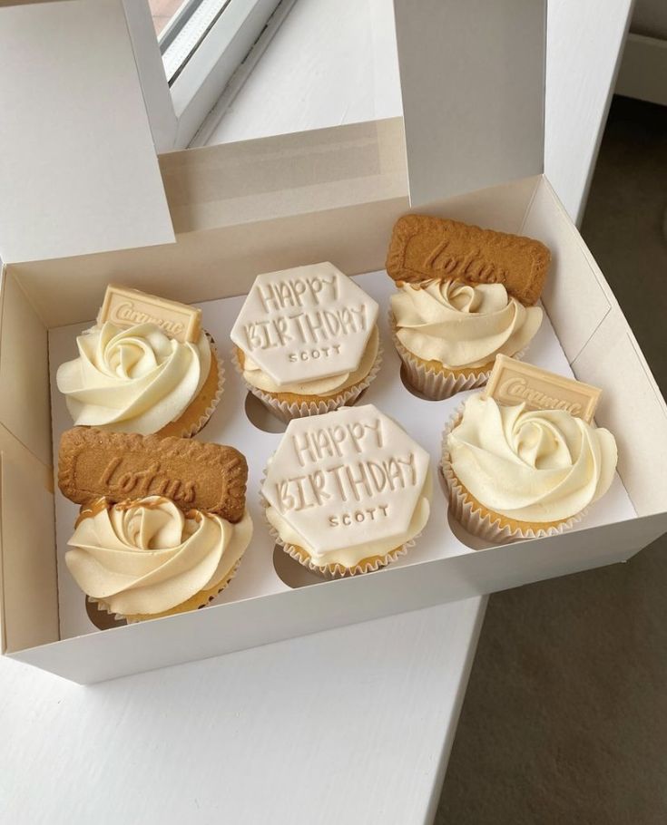 a box filled with lots of cupcakes on top of a white table next to a window