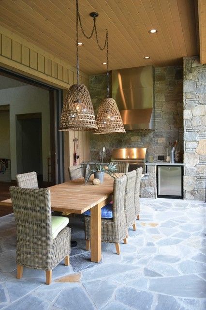 a dining room table with chairs and lights hanging from it's ceiling over an outdoor kitchen