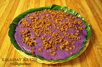 a purple dessert with crumbs on top is sitting on a wooden table next to a green leaf