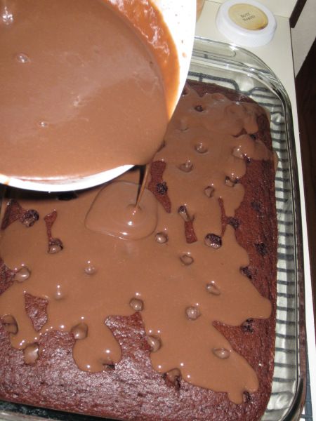 someone pouring chocolate sauce on top of a brownie in a pan with other items