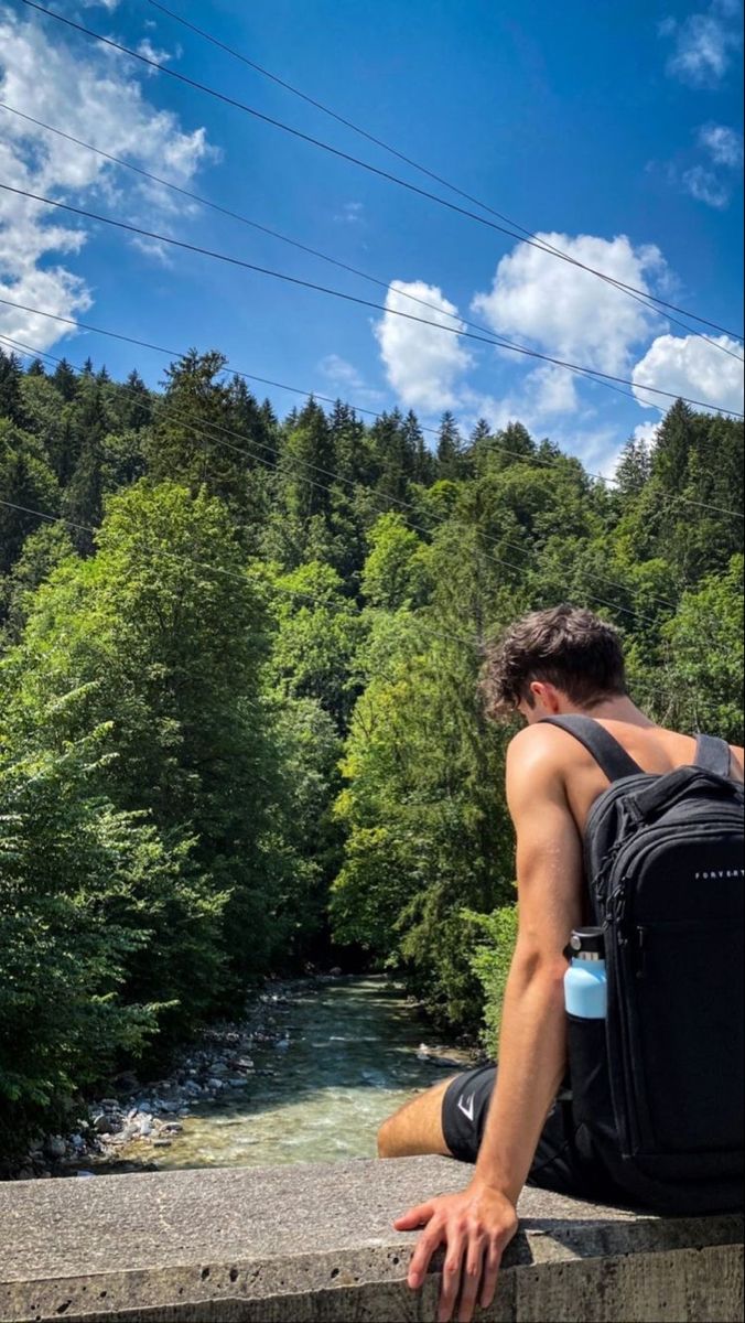 a man with a backpack sitting on a ledge next to a river