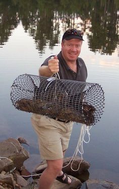 a man standing on top of a rock next to a body of water holding a bird cage