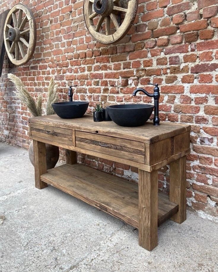 two sinks are on top of a wooden table in front of a brick wall with wheels