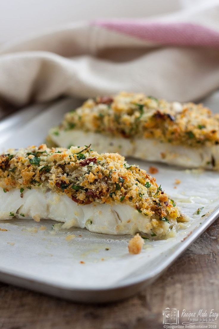 two fish fillets on a white plate with parmesan cheese and seasoning