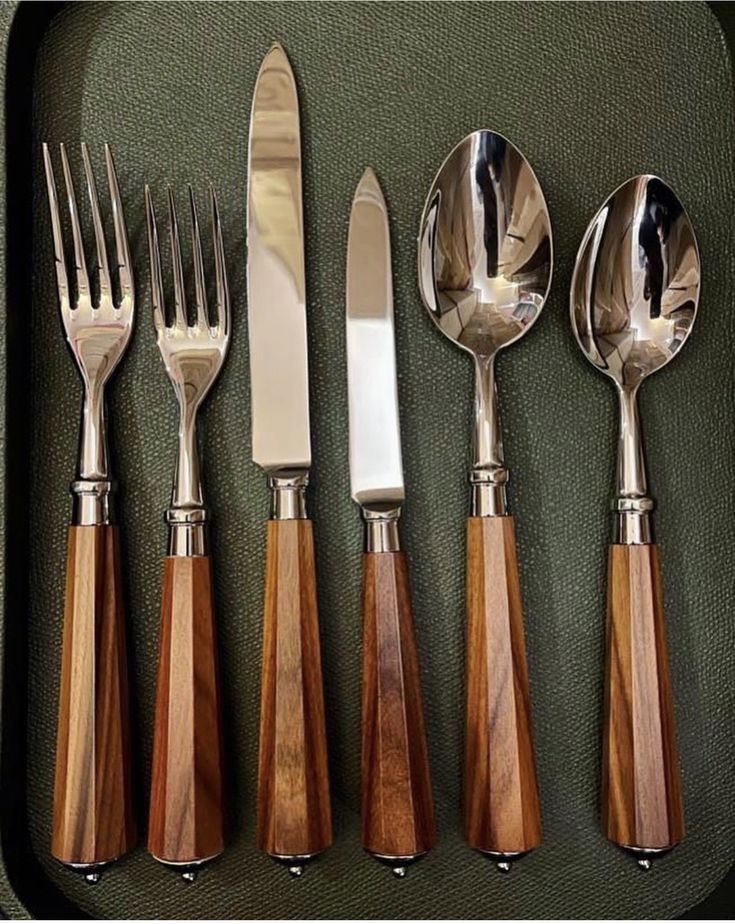 five forks, knives and spoons are arranged in a tray on a tablecloth