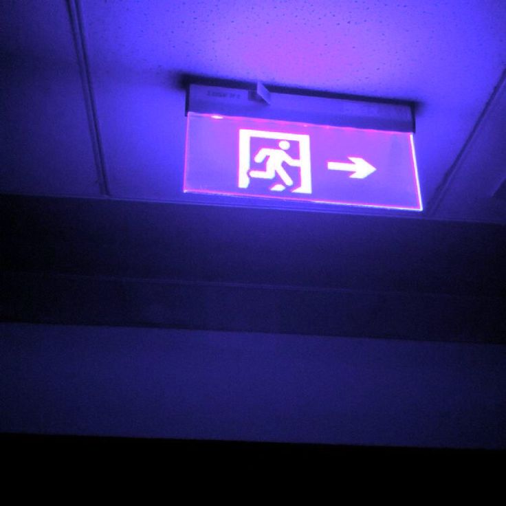 a purple sign with an arrow pointing to the left on a ceiling in a dark room