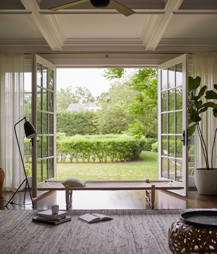 a living room with an open window looking out onto the yard and trees in the distance