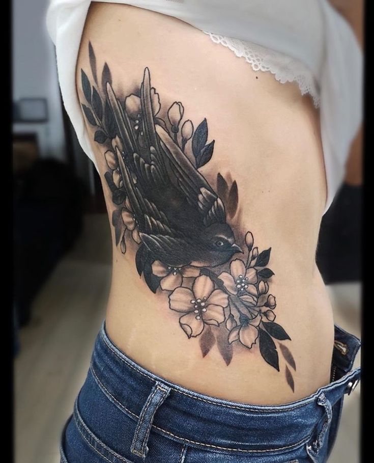 a woman's stomach with a bird and flowers tattoo on her side ribcage