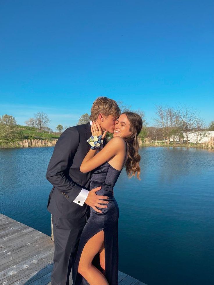 a man and woman are kissing on a dock by the water with their arms around each other