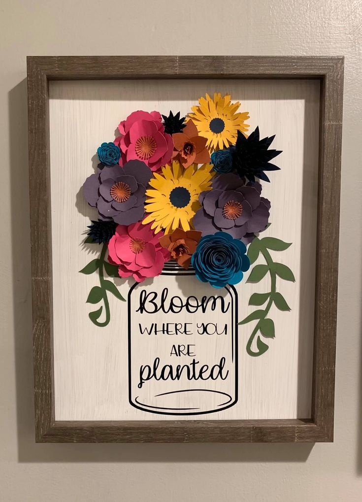 a wooden frame with paper flowers and the words bloom where you are planted