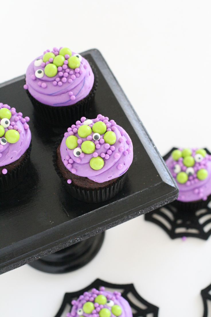 cupcakes with purple frosting and green sprinkles are on a black plate