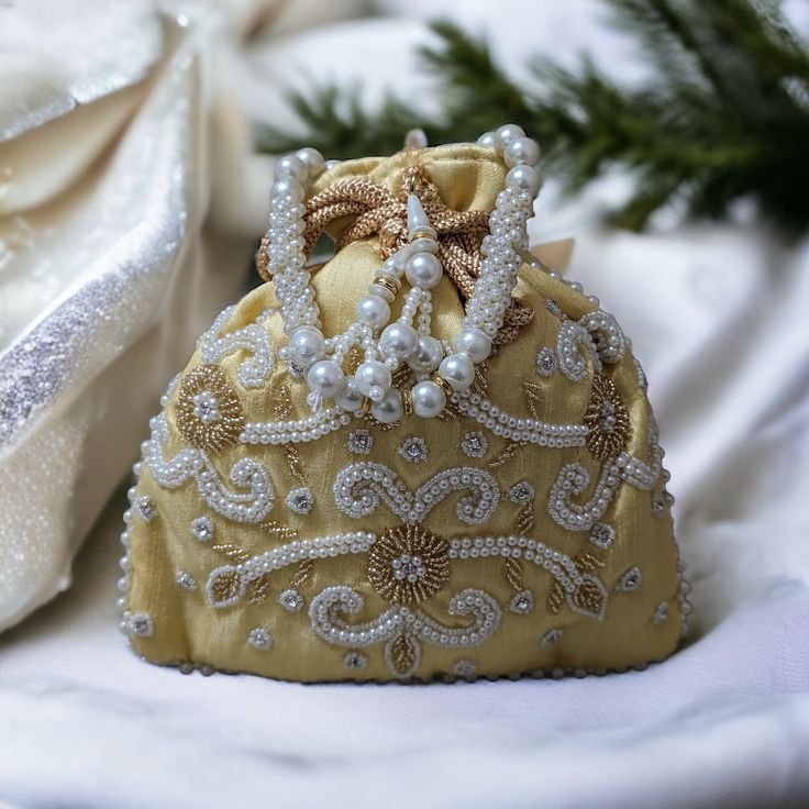 This exquisite handmade velvet potli bag is a true embodiment of elegance and tradition. Crafted from rich burgundy velvet, it features intricate gold embroidery and delicate pearl beadwork, creating a mesmerizing floral pattern. The bag is adorned with a decorative pearl handle and a golden drawstring, ensuring both style and practicality. Perfect for weddings, festive occasions, or adding a touch of glamour to any outfit, this potli bag is a timeless accessory that blends classic craftsmanship Luxury Embroidered Festive Bags, Luxury Embroidered Festive Bag, Festive Traditional Evening Bag With Pearl Embroidery, Traditional Festive Evening Bag With Pearl Embroidery, Elegant Evening Bags With Pearl Embroidery For Festivals, Festive Potli Bag With Gold Embroidery, Festive Gold Embroidery Potli Bag, Festive Luxury Evening Bag With Pearl Embroidery, Traditional Formal Bags With Pearl Embroidery