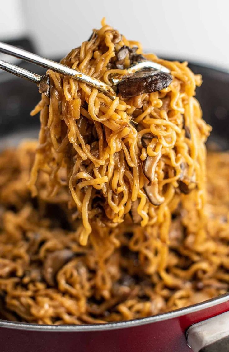 a spoon full of noodles and mushrooms being lifted from a pot with the noodles in it