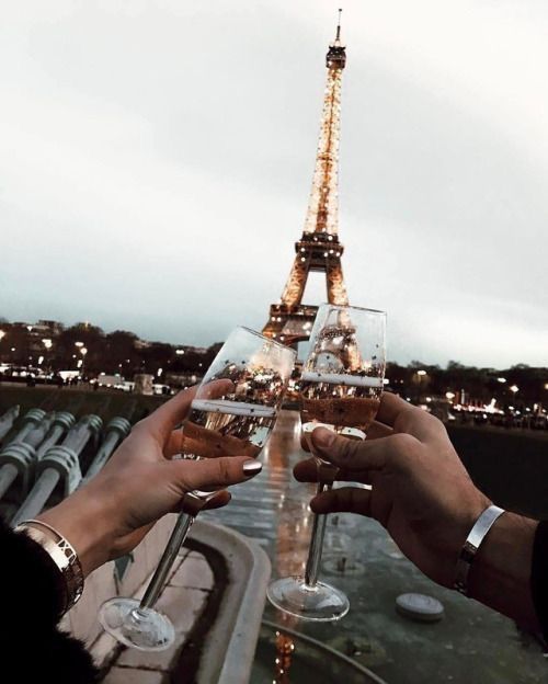 two people holding wine glasses in front of the eiffel tower