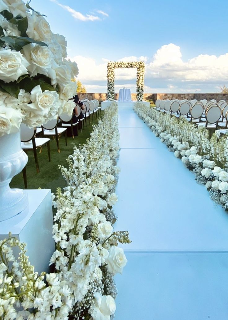 the aisle is lined with white flowers and chairs are set up for an outdoor ceremony