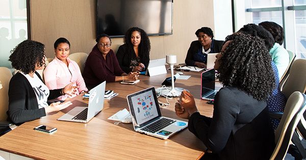 a group of people sitting around a conference table with laptops on each side of the table