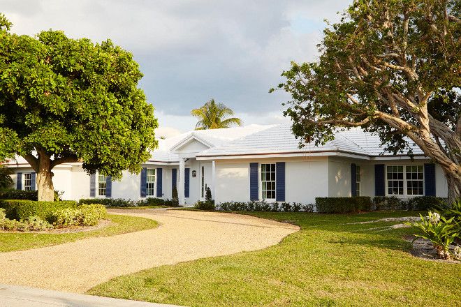 a white house with blue shutters and trees in the front yard on a cloudy day