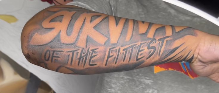 a man with a tattoo on his arm that says survival of the fittest