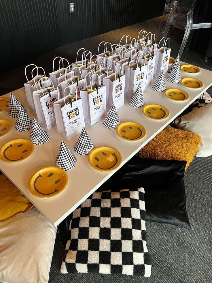 a table topped with paper bags filled with yellow smiley face decorations and black and white checkered pillows