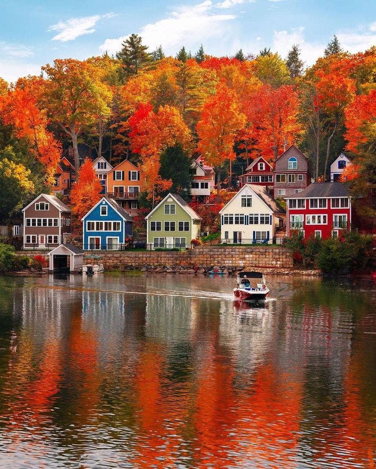 a boat traveling down a river next to colorful houses in the fall season with trees turning orange and red