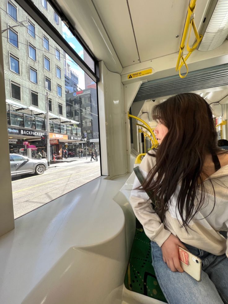 a woman is sitting on a bus looking out the window at the street below her