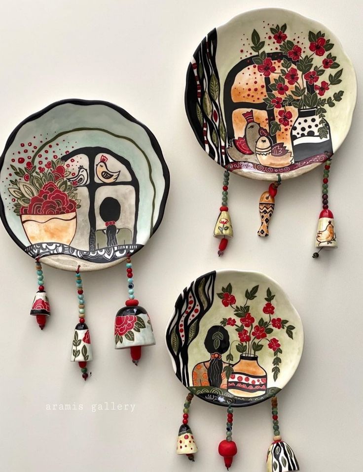 three plates with designs on them are hanging from the wall, and one has bells attached to it