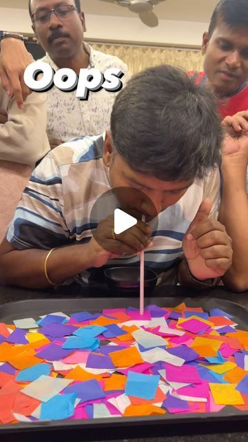 a man blowing out the candles on a cake that is decorated with multicolored paper