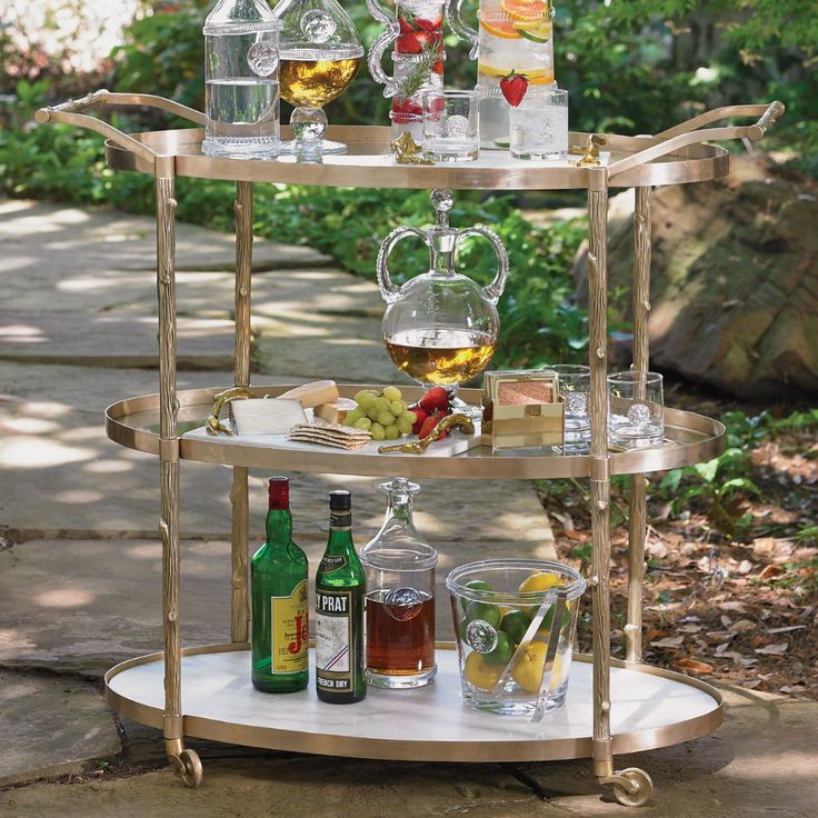 a three tiered serving cart with glasses and bottles on the top, sitting outside