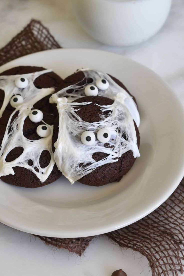 chocolate cookies decorated with white icing and spooky eyes are on a plate