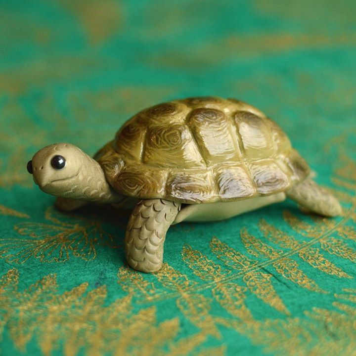 a small toy turtle sitting on top of a green tablecloth with gold leafy designs