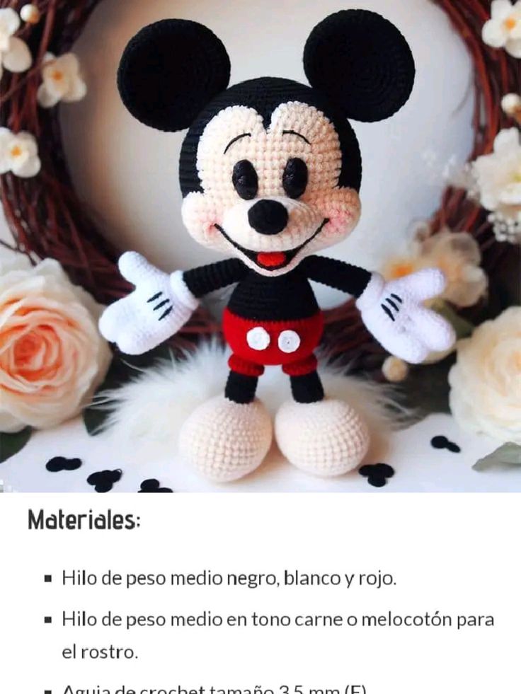 a crocheted mickey mouse is standing in front of a wreath with flowers on it