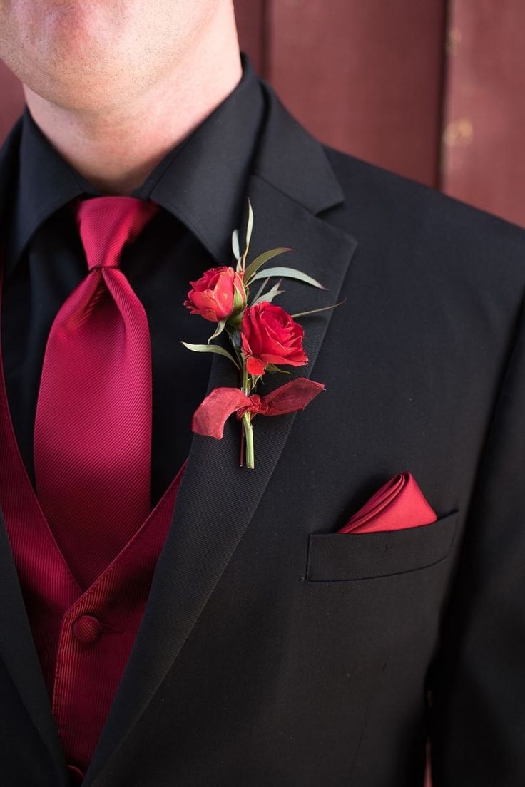 a man wearing a black suit with red flowers on it's lapel flower