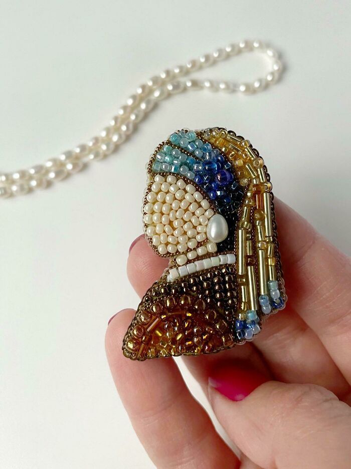 a hand holding a beaded brooch on a white background with pearls and beads