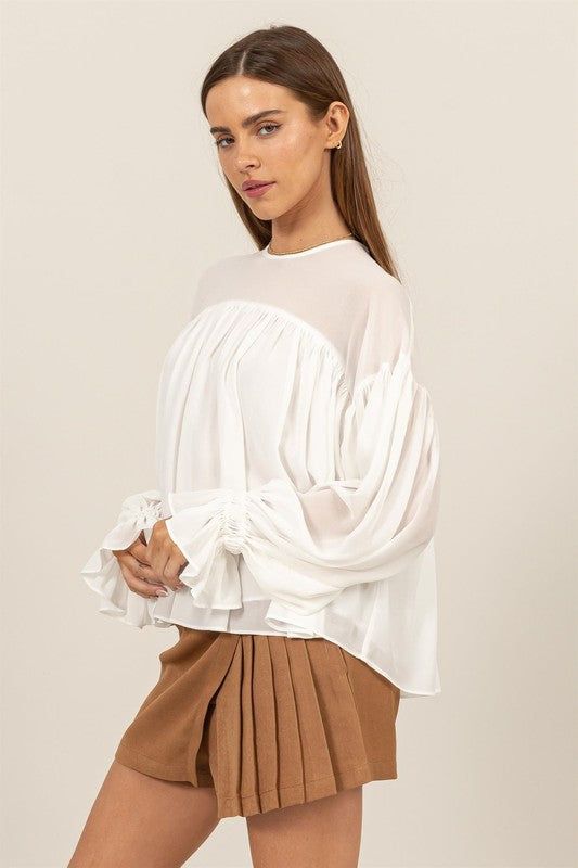 ELEVATE YOUR STYLE WITH THIS FLOWY LONG SLEEVE BLOUSE. FEATURING DRAMATIC GATHERED CUFFS AND A RELAXED, AIRY FIT, THIS BLOUSE OFFERS BOTH COMFORT AND ELEGANCE. PERFECT FOR A CASUAL DAY OUT OR A SPECIAL OCCASION, ITS UNIQUE DESIGN ADDS A TOUCH OF SOPHISTICATION TO ANY OUTFIT. White Casual Top With Sheer Sleeves, Casual White Tops With Sheer Sleeves, Casual White Top With Sheer Sleeves, Spring Blouse With Sheer Sleeves For Layering, White Long Sleeve Tops With Sheer Sleeves, Chic Blouse With Sheer Sleeves For Spring, White Blouson Sleeve Tops For Day Out, White Tops With Blouson Sleeves For Day Out, White Trendy Tops With Blouson Sleeves