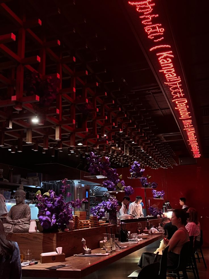 people sitting at tables in a restaurant with red lights on the ceiling and decorations hanging from the ceiling