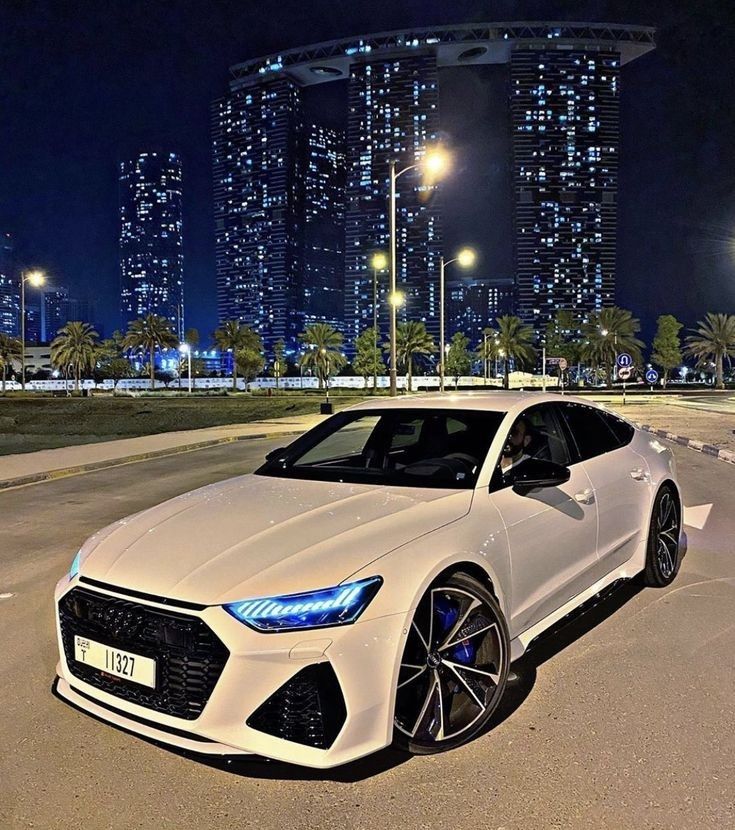 a white sports car parked in front of some tall buildings at night with its lights on