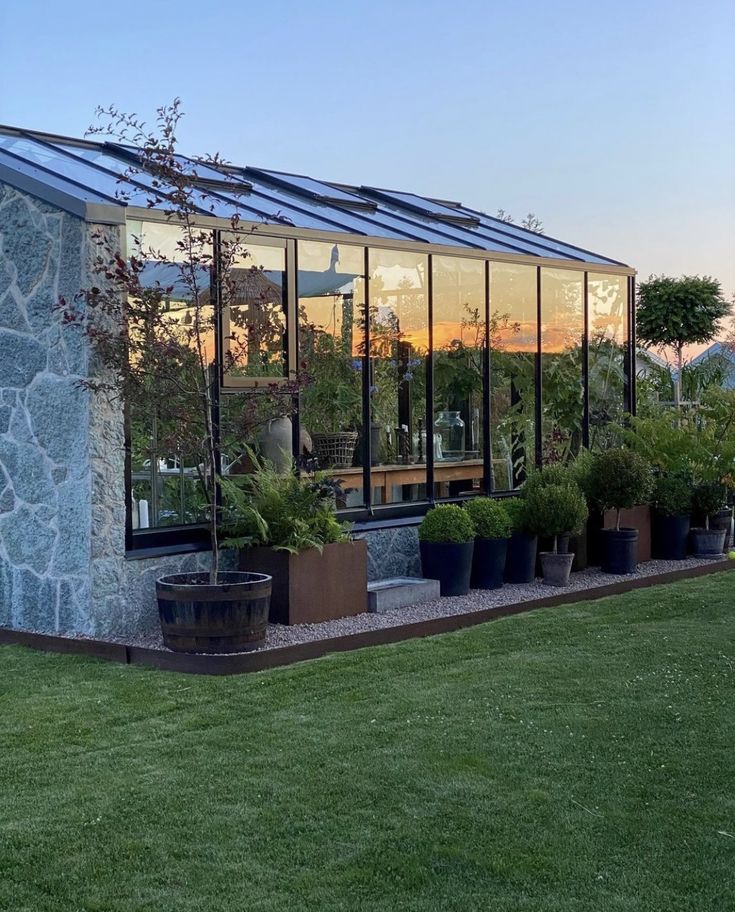 a house with many plants in front of it and the sun setting on the other side