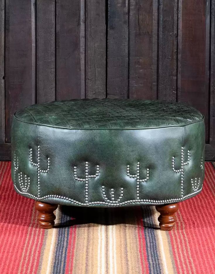 a green leather ottoman sitting on top of a striped rug next to a wooden wall